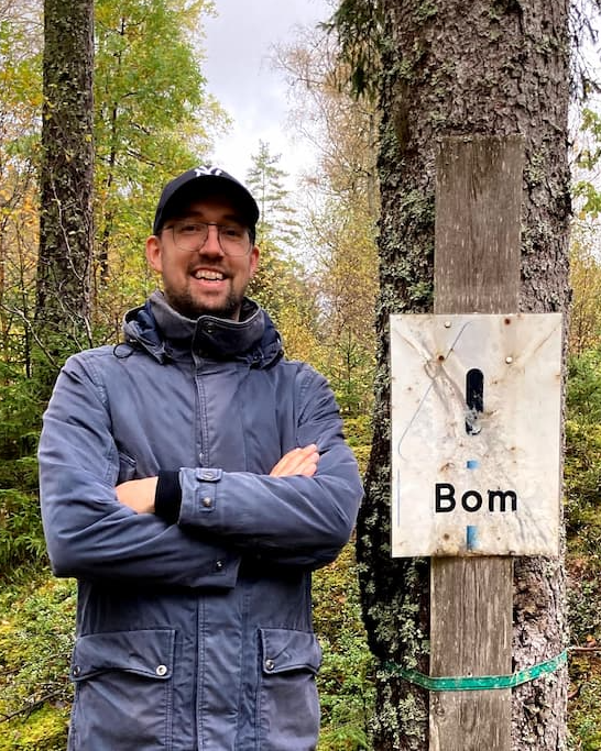 Niels Bom standing in a forest, in front of a sign that says 'Bom'.